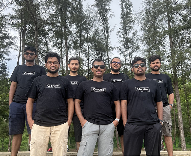 Group of men wearing matching "Orviko" t-shirts, standing in front of trees, smiling at the camera.
